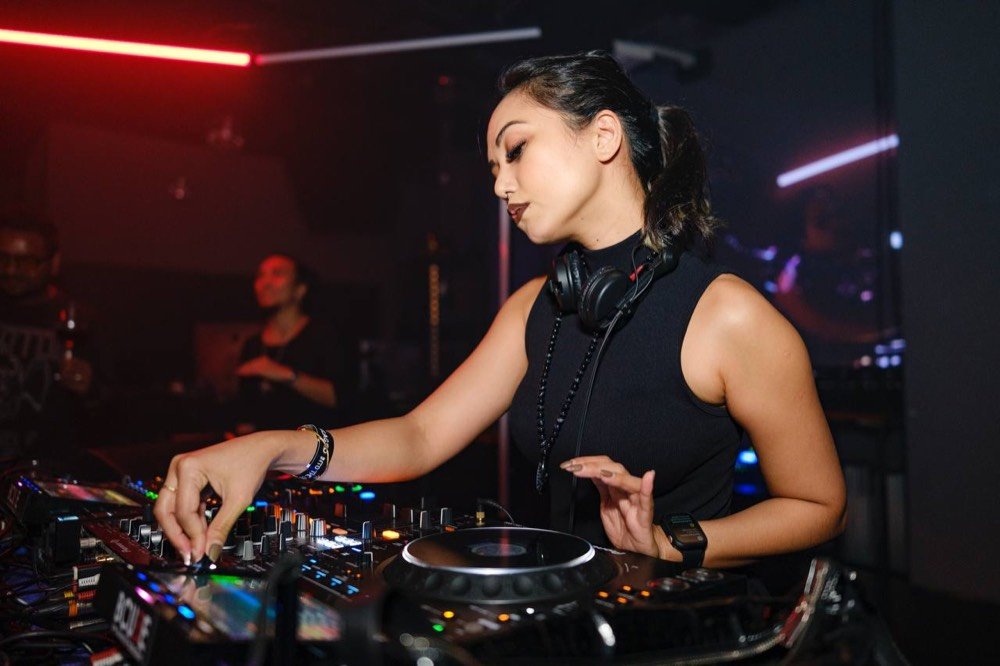 Mixing at the CDJs in a dark booth, red and violet neon behind her